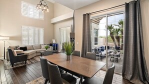 A spacious living area with a dining table, sofa, and a view of the outdoors through large windows. - Northstar Zen Resort: Rock Waterslide Pool, Spa, MultiBall Zone & Game Room (Glendale)