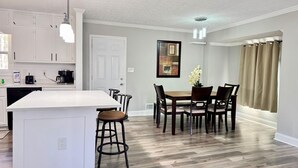 Una cocina moderna con armarios blancos, una isla central y un comedor con mesa y sillas.