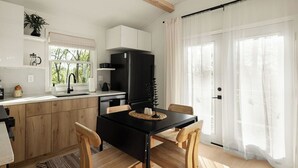 A modern kitchen with wooden cabinets, a black refrigerator, and a dining table with chairs. - NEW Zen Cabin in the Clouds . Hot Tub, Wineries, Skyline  (Front Royal)