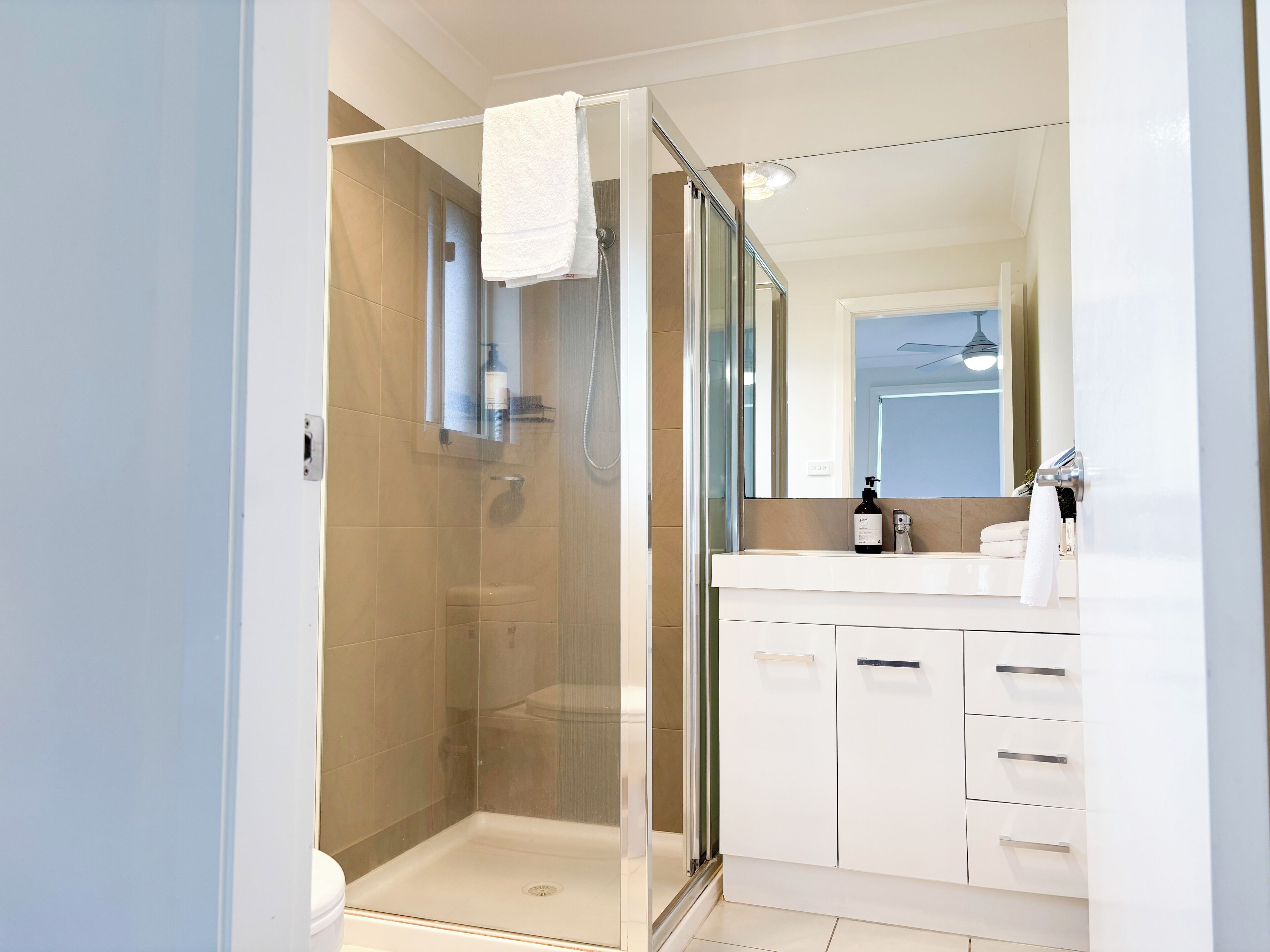 A modern bathroom with a glass-enclosed shower, a white vanity with a mirror, and a toilet.