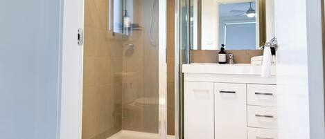 A modern bathroom with a glass-enclosed shower, a white vanity with a mirror, and a toilet.