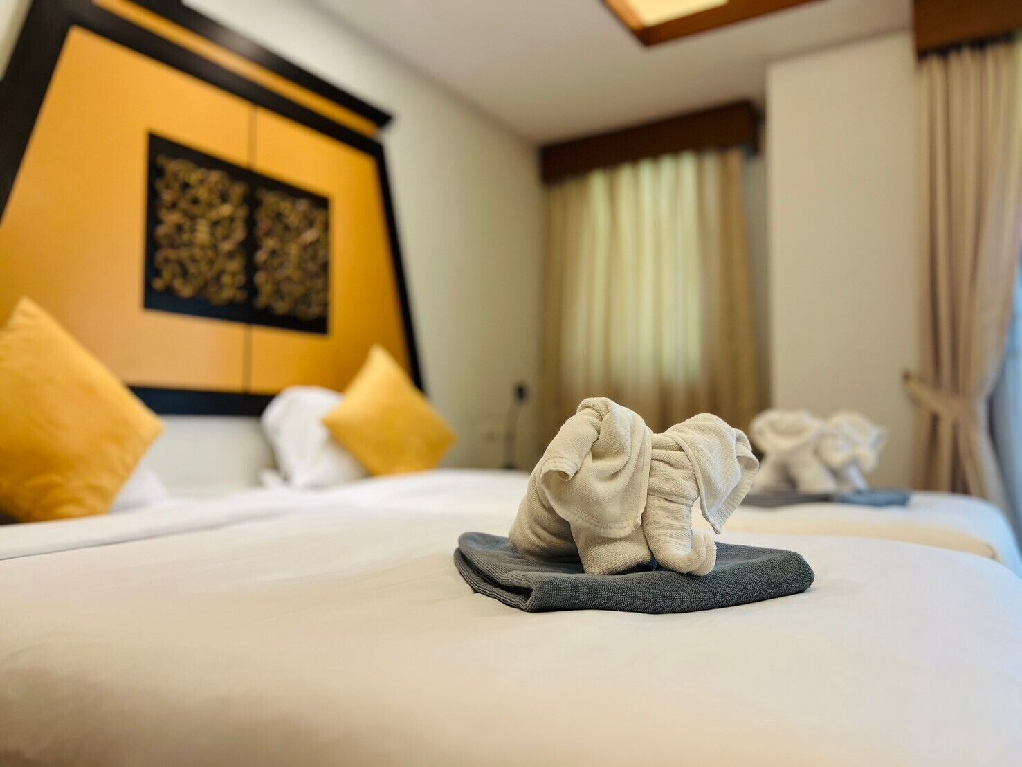 Una camera d'albergo con un letto rifatto, una testiera decorata e una finestra con tende.