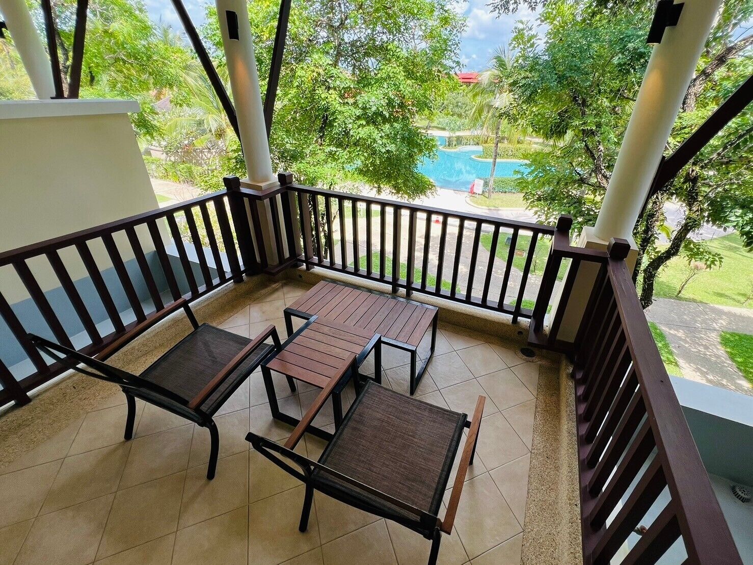 Un balcon donnant sur une piscine, le tout entouré de verdure.