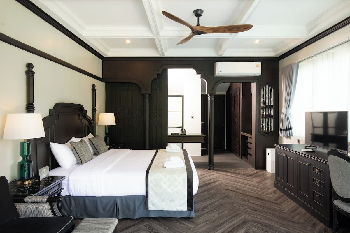 A hotel room with a large bed, bedside tables, a desk, a chair, a ceiling fan, and a television.