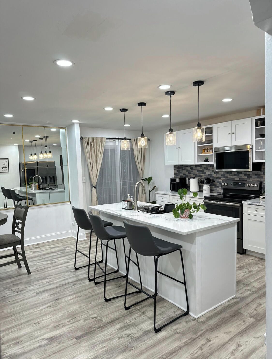 A modern kitchen with a central island, bar stools, pendant lighting, and a view into the dining area.