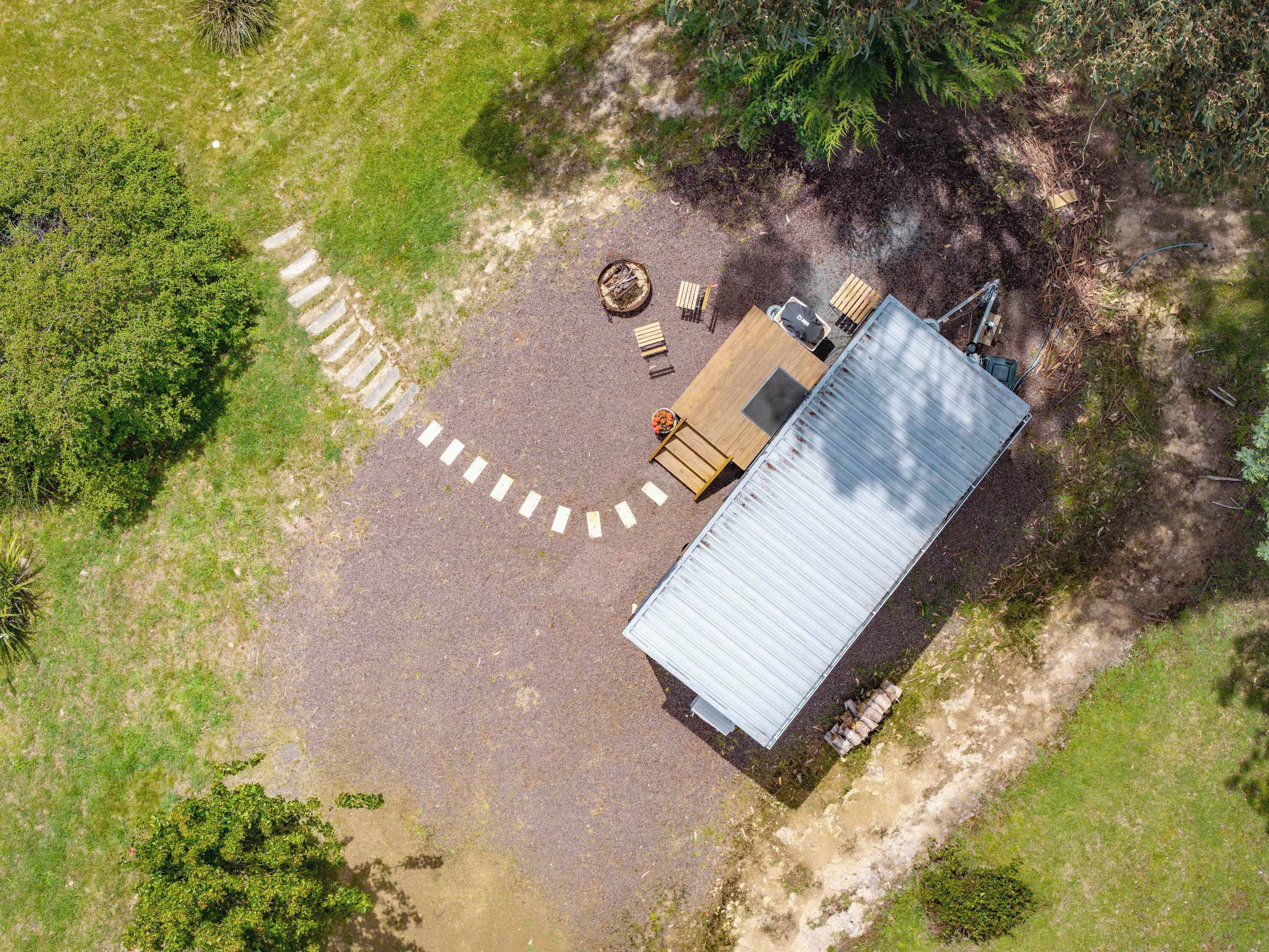 An aerial view of a property with a metal-roofed building, a paved driveway, and a wooden deck with outdoor furniture.