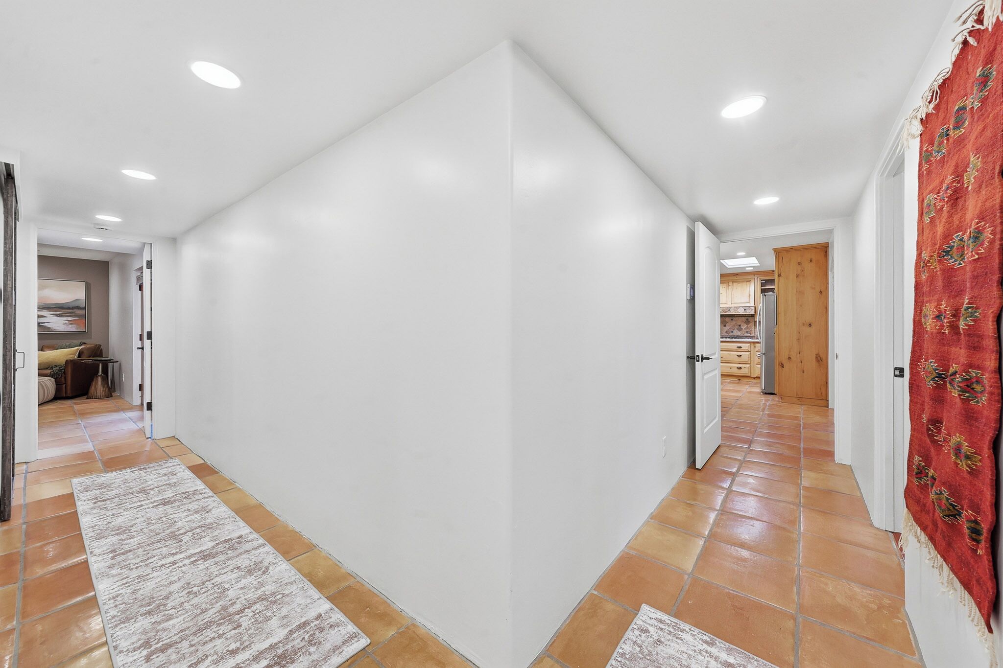 A hallway with white walls, a tiled floor, and a red patterned rug.