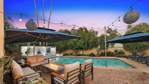 A poolside area with outdoor seating, string lights, and umbrellas.