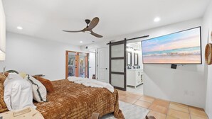 A bedroom with a bed, a ceiling fan, a TV, and a sliding door leading to a bathroom.