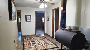 A hallway with a wooden floor, a patterned rug, a ceiling fan, and a large cylindrical object, possibly a heater, on the right.