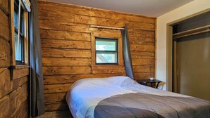 A bedroom with a bed, a window, and a wooden wall.
