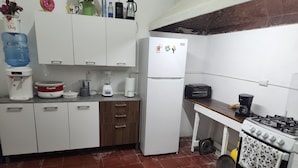 A kitchen with white cabinets, a stove, a refrigerator, and various appliances like a water dispenser and a coffee maker.
