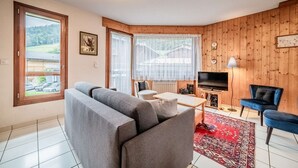 A cozy living room with a grey sofa, a blue armchair, a TV, and a red patterned rug.