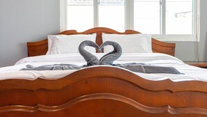 A bed with a wooden headboard and two towels arranged in a heart shape.