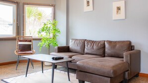 A living room with a brown sofa, a wicker chair, a small table, and a potted plant.