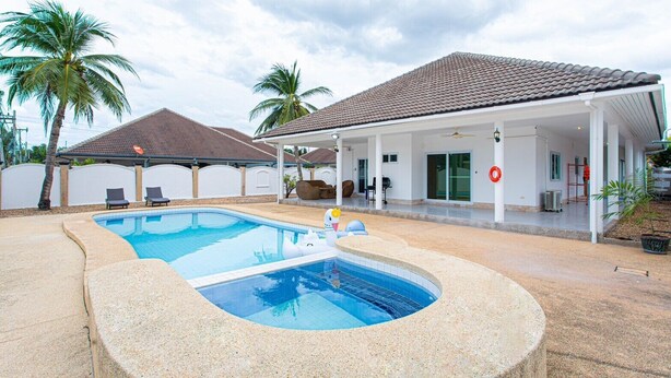 A swimming pool with a hot tub, lounge chairs, and a covered patio area.