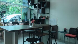 Ein Café mit einem langen Tisch, Stühlen, einem Bücherregal und einem kleinen runden Tisch mit einem roten Stuhl.