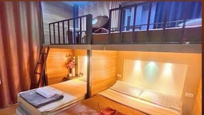 Ein Zimmer mit zwei Betten, einem hölzernen Kopfteil, einem kleinen Tisch mit einer Vase und einem Fenster mit Vorhängen.