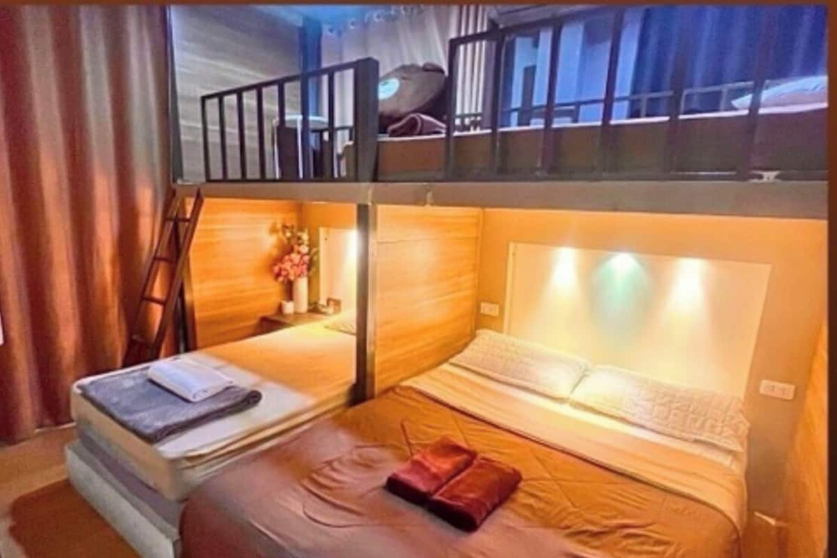 A room with two beds, a wooden headboard, a small table with a vase, and a window with curtains.