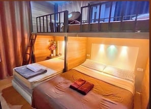 Una habitación con dos camas, cabecero de madera, una mesita con un florero y una ventana con cortinas.