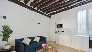 A modern living room with a blue sofa, wooden coffee table, and a kitchen area with white cabinets and a microwave. - Relaxing Urban Getaway, Notre Dame de Paris (Paris)