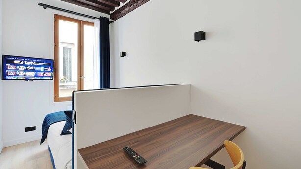 A modern room with a wooden desk, a single chair, a TV mounted on the wall, and a window with curtains. - Relaxing Urban Getaway, Notre Dame de Paris (Paris)