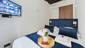 A hotel room with a bed, a TV mounted on the wall, a wooden headboard, and a tray with fruits and a vase of flowers. - Relaxing Urban Getaway, Notre Dame de Paris (Paris)