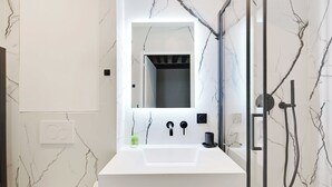 A modern bathroom with a white marble sink, a large mirror, and a glass-enclosed shower. - Relaxing Urban Getaway, Notre Dame de Paris (Paris)