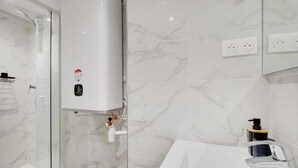 A modern bathroom with a glass shower enclosure, a white sink, and marble-patterned walls. - Intimate Apartment - 2P - Le Marais (Paris)