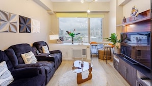 Una sala moderna con sofá, mesa de centro y televisor. Se ve una ventana con vistas a la ciudad.