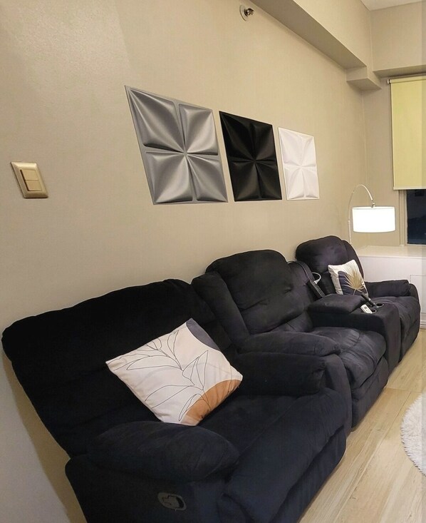 A living room with a black sofa, a white lamp, and three wall-mounted decorative panels.