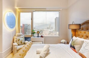 Une chambre d’hôtel avec un grand lit, un miroir rond, une table de chevet et une fenêtre donnant sur la ville.