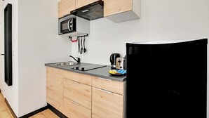 Una cocina compacta con un refrigerador negro, un microondas, una cafetera y armarios de madera.