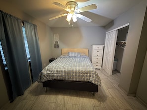 Un dormitorio con cama, mesita de noche, cómoda, ventilador de techo y armario.