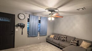 Un salon avec un canapé, un ventilateur de plafond, une horloge et une porte.