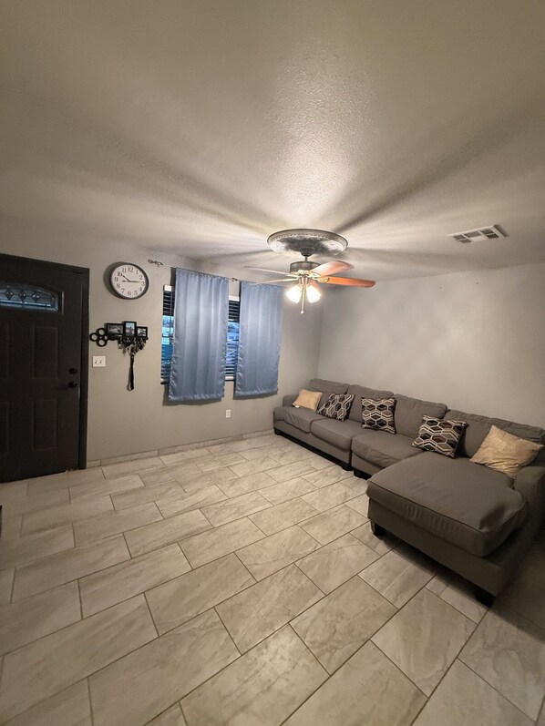 A living room with a sofa, a ceiling fan, a clock, and a door.