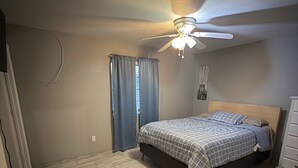 Une chambre à coucher avec un lit, un ventilateur de plafond et une fenêtre avec des rideaux.