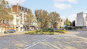 Een geplaveid straatbeeld met historische gebouwen, een standbeeld en een modern gebouw op de achtergrond.