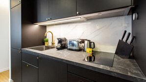 A modern kitchen with dark cabinets, a marble countertop, a coffee maker, a toaster, and a kettle.
