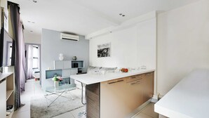 A modern kitchen with a central island, built-in cabinets, and a dining area with a glass table. - Cosy Apartment - 1br/4p - Gare Saint-lazare (Paris)