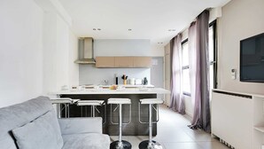 A modern kitchen with a central island, bar stools, and a grey sofa. - Cosy Apartment - 1br/4p - Gare Saint-lazare (Paris)
