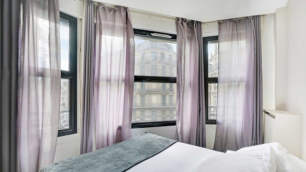 A hotel room with a bed, a window with curtains, and a view of a building outside. - Cosy Apartment - 1br/4p - Gare Saint-lazare (Paris)
