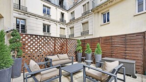 An outdoor patio with a sofa, chairs, and tables, surrounded by a wooden fence and potted plants. - Cosy Apartment - 1br/4p - Gare Saint-lazare (Paris)