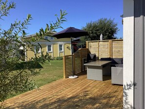 Una terraza de madera con mobiliario exterior, una pérgola y vista a una casa.