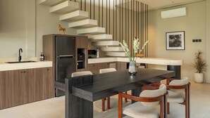 A modern kitchen with a dark countertop, wooden cabinets, a built-in refrigerator, and a staircase with a unique design. - Villa Mesra Stunning Paddy Fields Views - Canggu Berawa (Bali)