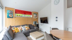 A modern living room with a grey sectional sofa, a wooden coffee table, and a TV mounted on the wall. - Holiday Home in Sint Maartenszee (Sint Maartensvlotbrug)