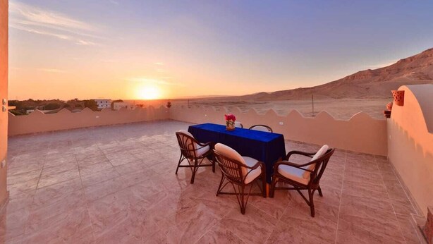 A terrace with a table and chairs, overlooking a desert landscape at sunset. - One-Bedroom Apartment (Luxor)