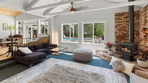 A spacious living room with a fireplace, large windows, and a view of a pool. - Shangri-La Sonoma - 5BR 4BA Redwood Retreat w/Heated Pool (Sebastopol)