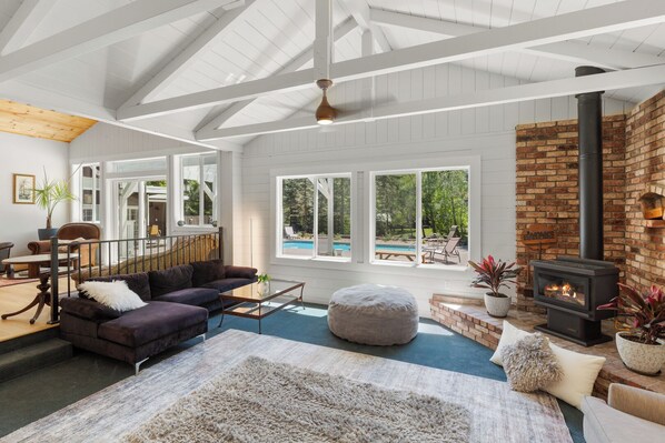 A spacious living room with a fireplace, large windows, and a view of a pool.