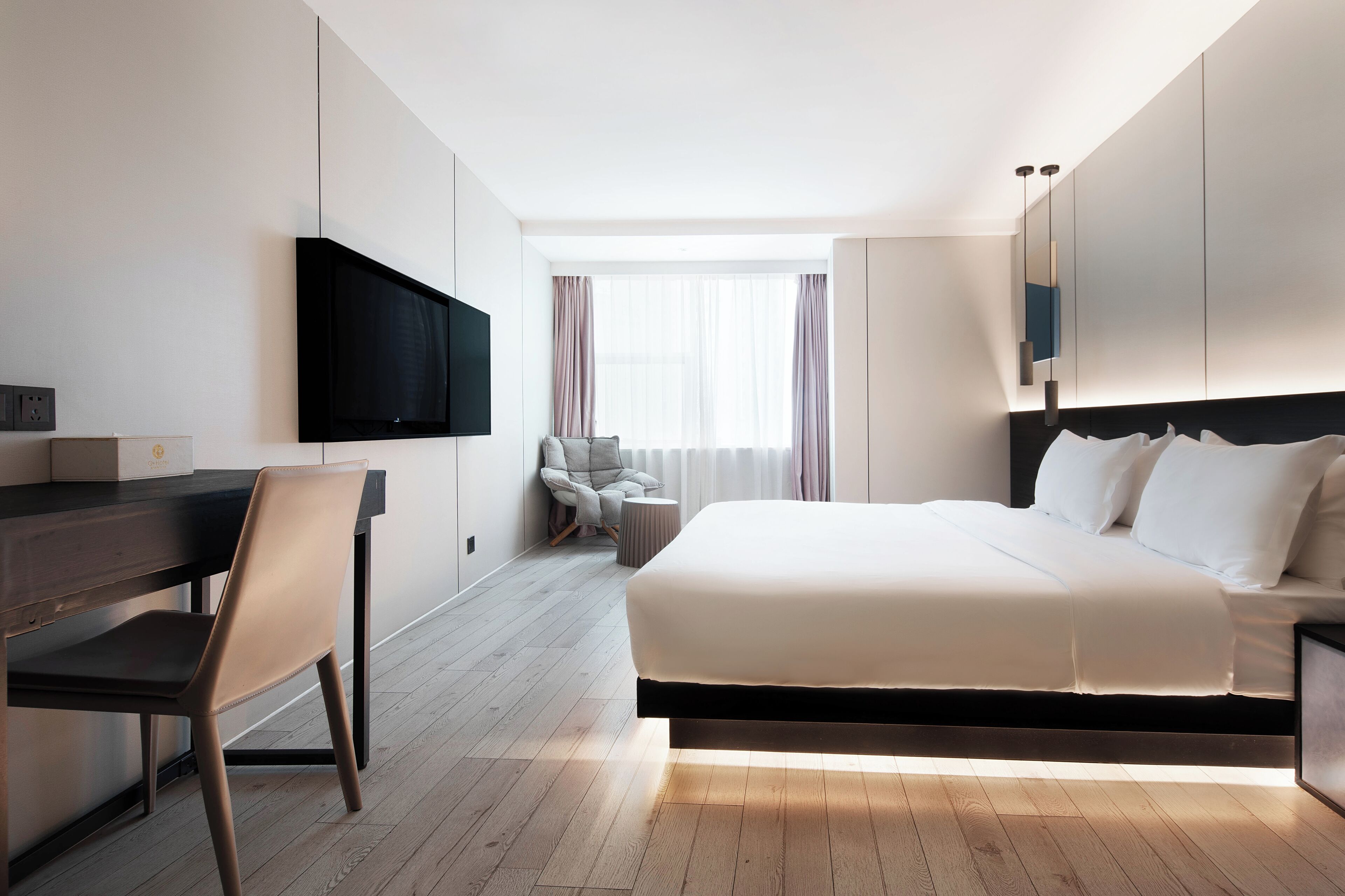 Una habitación de hotel moderna con cama, escritorio, silla, televisor y ventana con cortinas.
